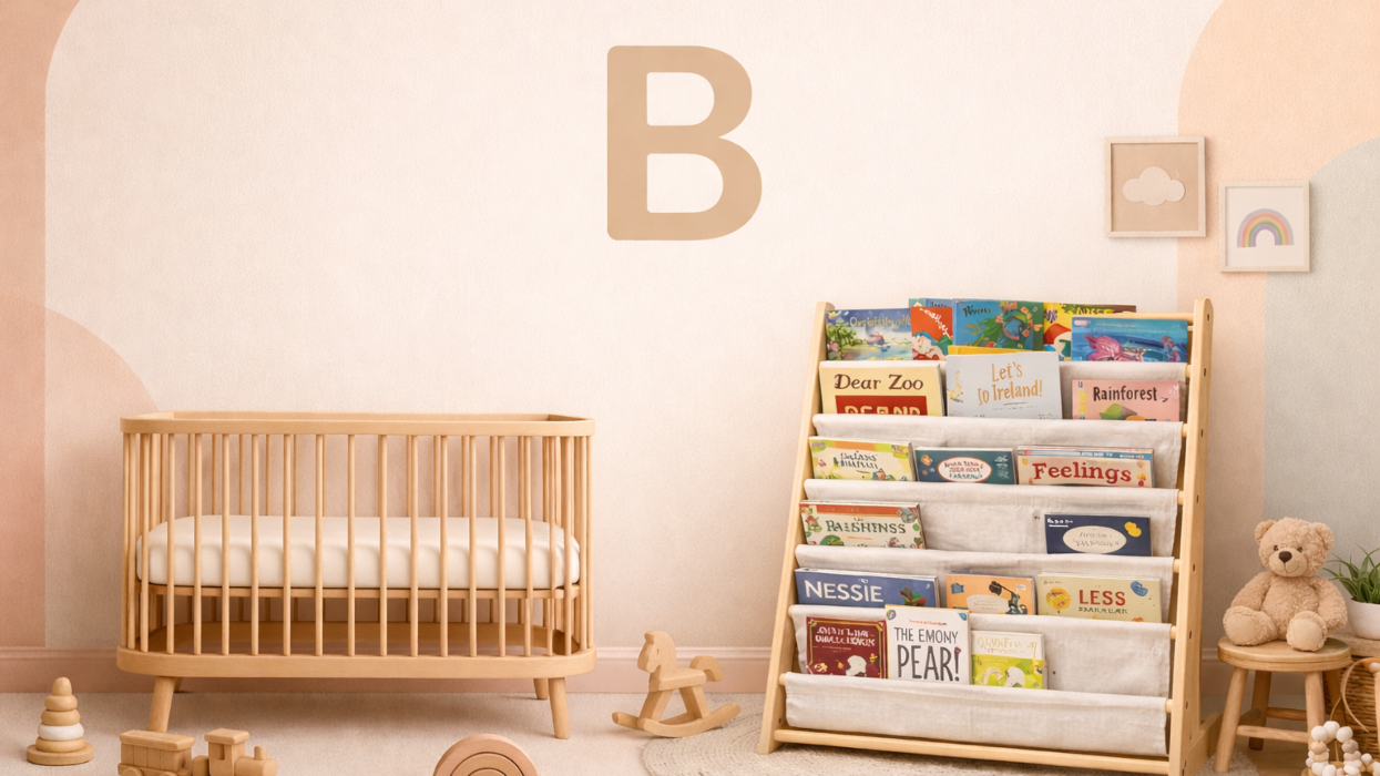 Children's room with wooden crib, bookshelf, and toys against a light pink wall.
